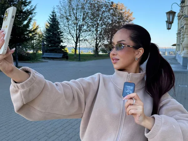 Девушка в бежевой флиске снимает селфи на улице