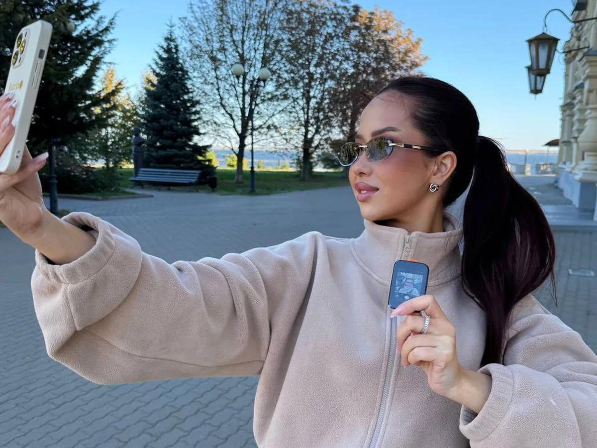 Девушка в бежевой флиске снимает селфи на улице